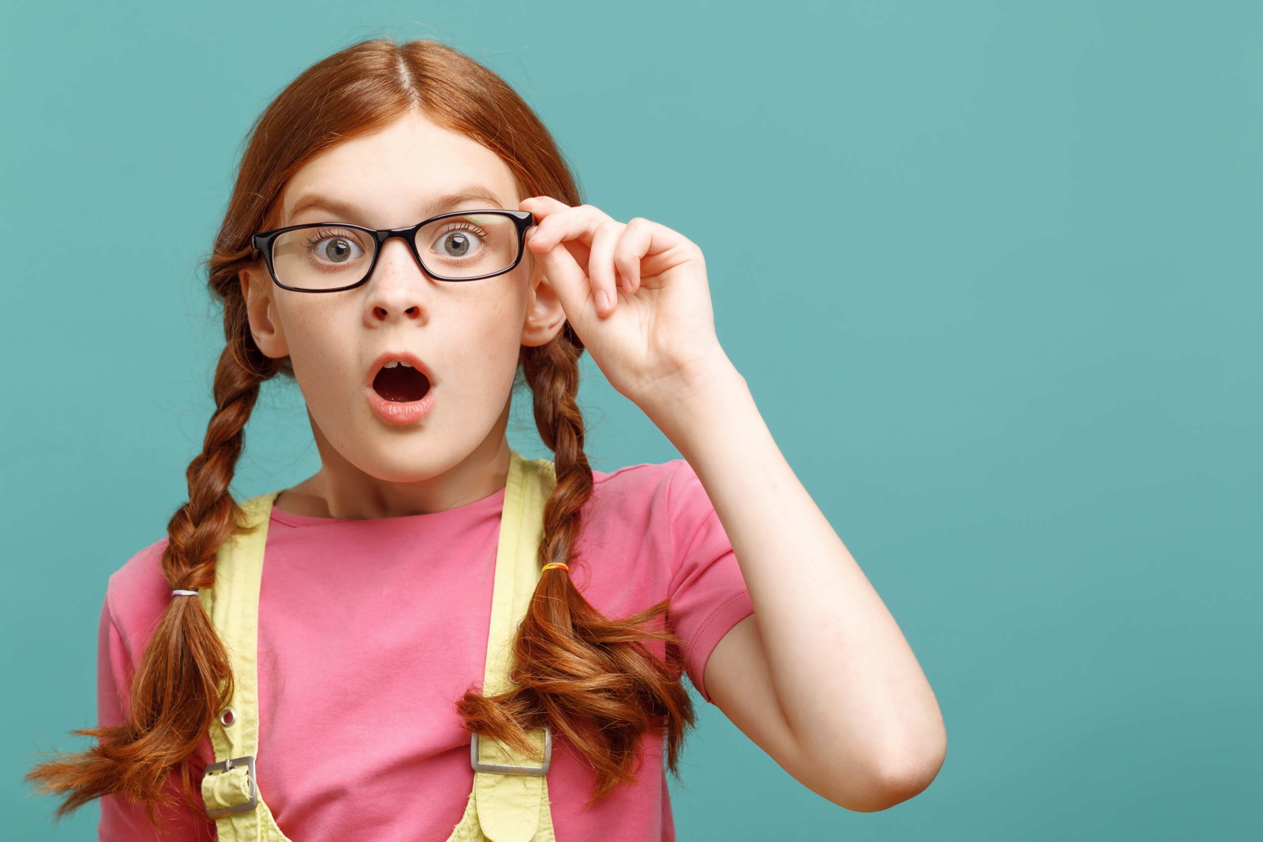 Grande merveille. Gros plan d'une petite fille rousse étonnée tenant des lunettes et regardant tout droit montrant la surprise.